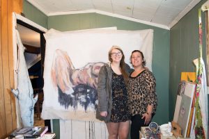 Hannah Malone and Sara Scott pose in front of one of Malone's eight feet figure paintings. Malone is a junior studio art major and the Director of Residents at Reckless Arts.