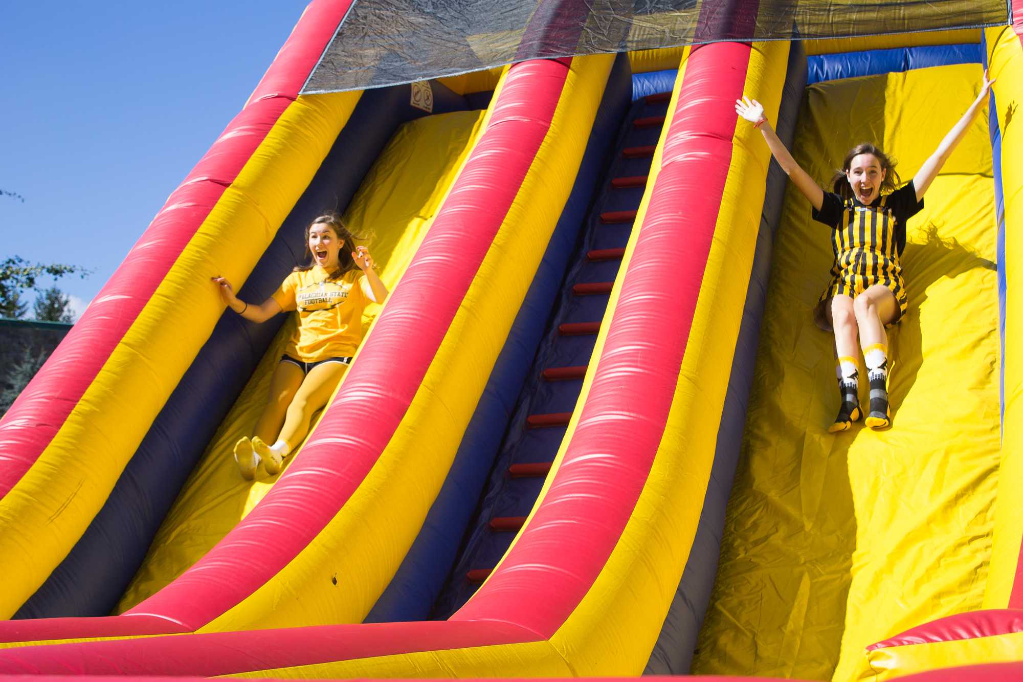 Freshman theater arts major Maddie Coggin (left) and freshman sustainable development major Devyn Barron (right) dress up to show their Mountaineer pride and enjoy the slides set up for Mountaineer Spirit Day on Oct. 19.