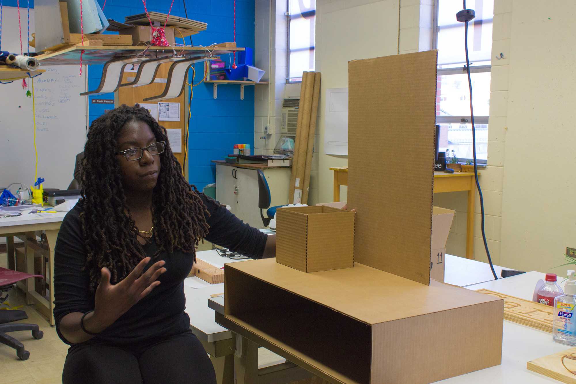 Senior industrial design major Sheilla Sanon explains her capstone project. The cardboard is a model for a shelf with a drawer, box and mirror. She describes it as a character furniture piece that describes her and her brother. Photo by Dallas Linger, Photo Editor