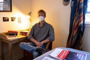 Lachlan James, head of the App State Chapter of IYSSE sits in his bedroom with hisi collection of literature and signage related to the world views represented in the organization.