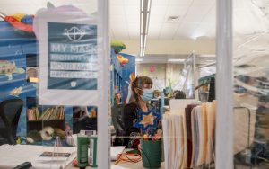 “It’s been like a little reunion”: Judith Winecoff, youth services librarian at the Watauga County Public Library, works at her desk behind plexiglass dividers to protect both employees and returning library patrons from COVID-19. 