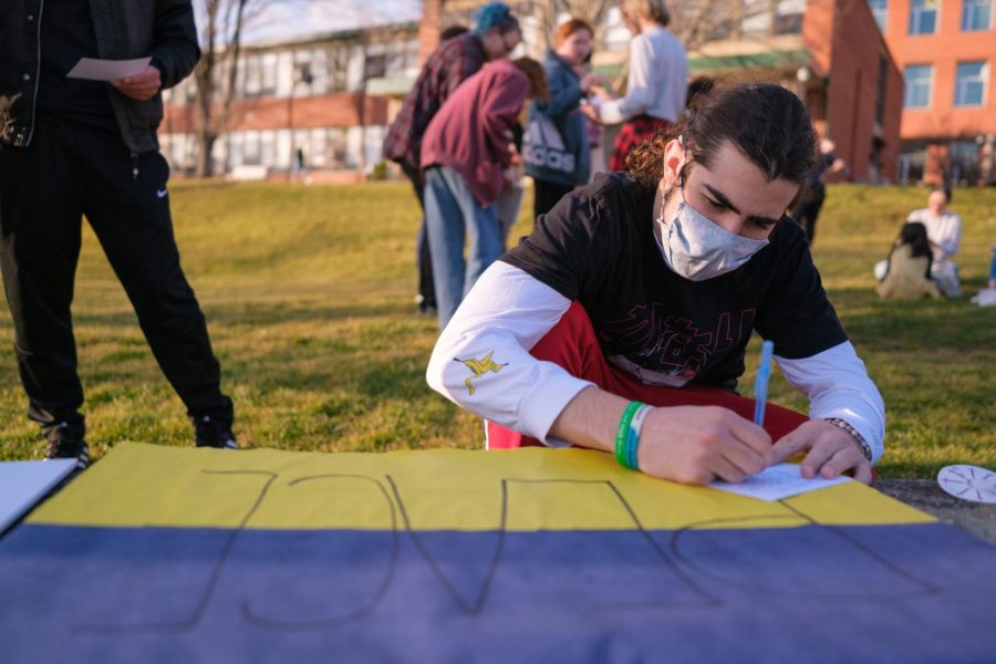  Student Lucas Blanco writes a letter to Ukrainians atop a homemade sign during the vigil Thursday, March 17, 2022.