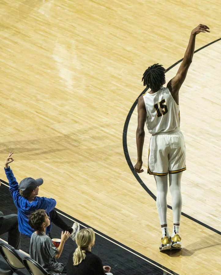 Junior forward CJ Huntley shoots a three-pointer while a young fan holds up three fingers in anticipation of the shot going in against Campbell Nov. 18, 2022.