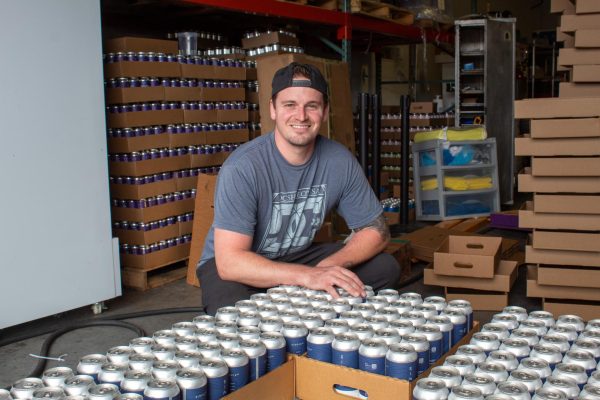 Joseph Meehan, the creator of Simple Wtr, posing by boxes of finished Simple Wtr cans to be sent off for distribution. Meehan started the company in May of 2022 and distributes his products to several local businesses.