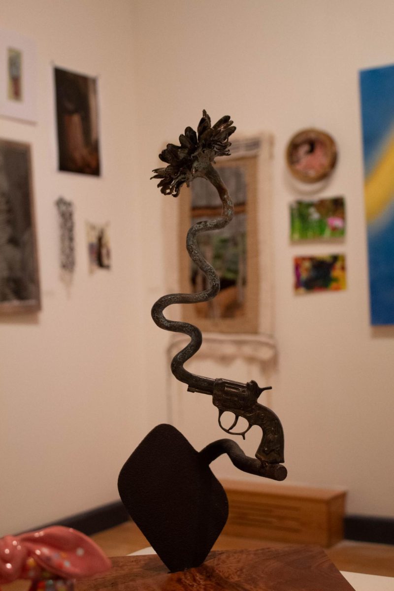 This multi item sculpture is named  “Gun #3 Reimagine”. The artist, (Mandy Bass) made this sculpture from bronze, some found objects, and spanish cedar wood.  
