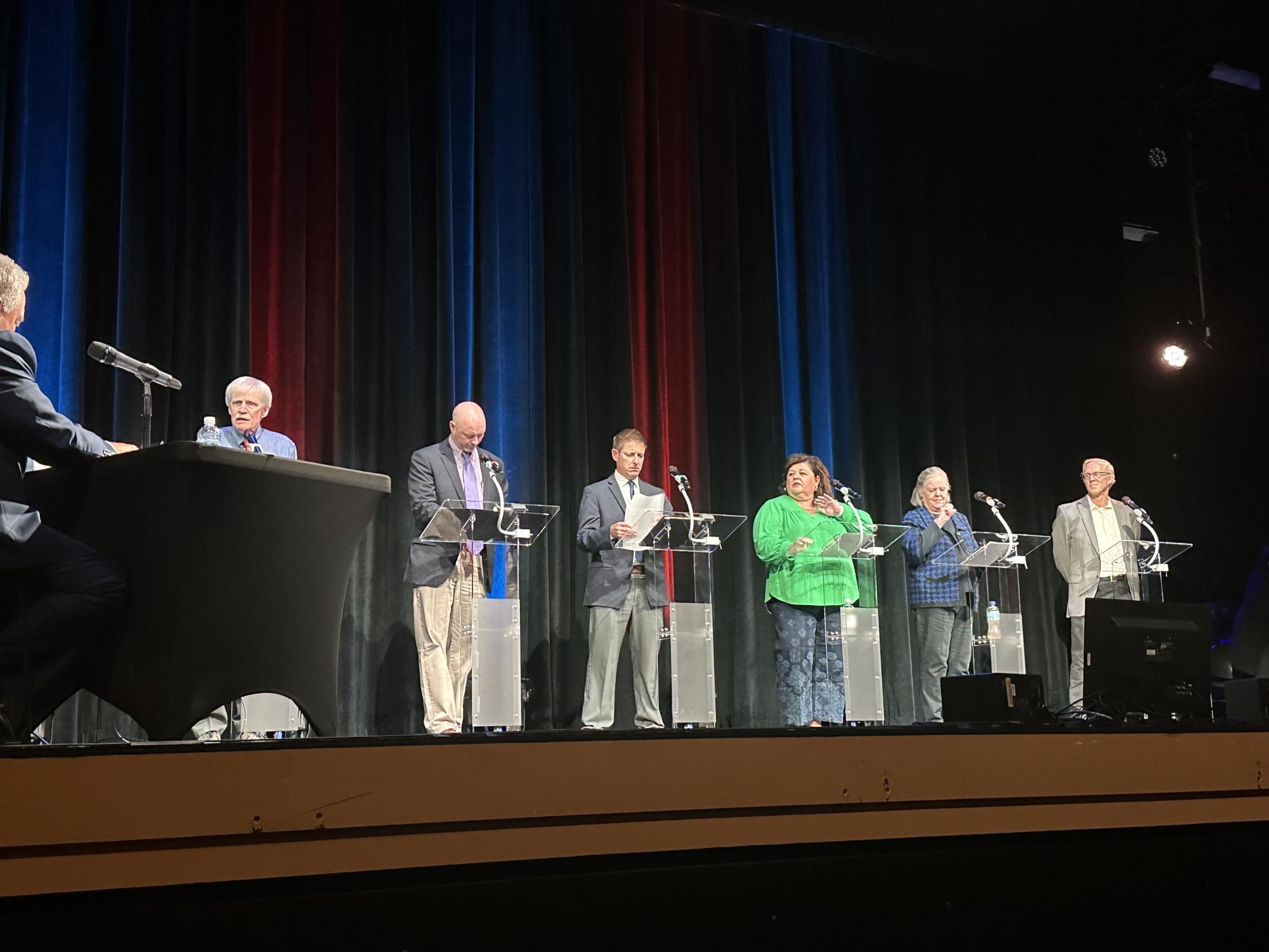 From left, Watauga County Board of Education candidates Marshall Ashcraft, Chad Cole, Adam Hege, Allison Idol, Charlotte Mizelle Lloyd, and Tom Ross stand onstage at the Appalachian Theatre of the High Country on Sept. 16.