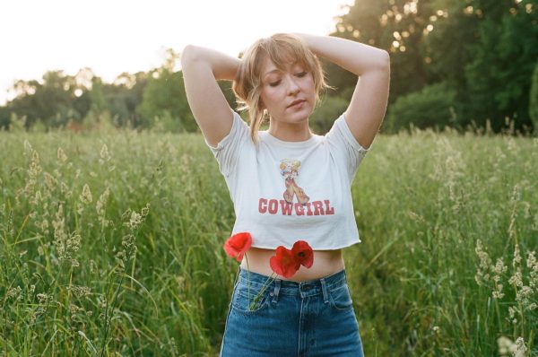 Country-folk musician Alexa Rose poses in a field with flowers in her jeans. Rose is originally from West Virginia and is following in her great grandfathers footsteps as a musician. Courtesy of Brandon Holder